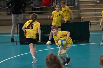 chłopiec w zółtej koszulce trzyma oburącz piłkę i biegnie