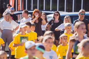 Na pierwszym planie grupa dzieci ubranych na żółto, w tle dorośli, jedna kobieta robiąca zdjęcie telefonem