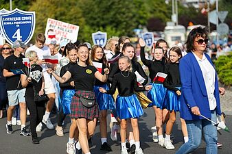 Uśmiechnięte dziewczęta idące w pochodzie z polskimi flagami, reprezentujące Szkołę Podstawową nr 4
