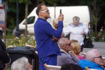 Mężczyzna w niebieskim ubraniu stojący pomiędzy publicznością i nagrywający występ