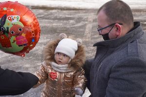 Małe dziecko z serduszkiem WOŚP, trzyma balonik. Obok stoi ojciec