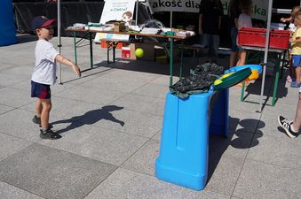 Korowe pojemniki do segregacji śmieci, mały chłopiec stojący niedaleko pojemników, w tle stoiska z książkami