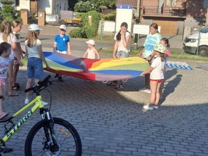 Dzieci trzymaące kolorową płachtę do zabawy.