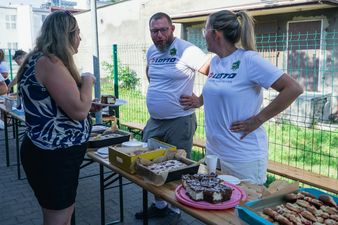 Organizatorzy festynu w białych koszulkach z logo klubu przygotowujący poczęstunek dla uczestników przy stole z ciastami