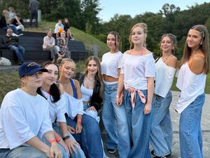 18. Grupka dziewczyn w białych koszulkach i dżinsach tańczy na chodniku przed sceną. 