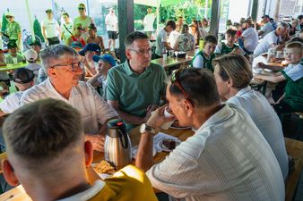 Uczestnicy festynu, w tym dorośli i dzieci, siedzący przy ławach podczas wspólnego posiłku, z widocznym na pierwszym planie termosem i ciastem na talerzu