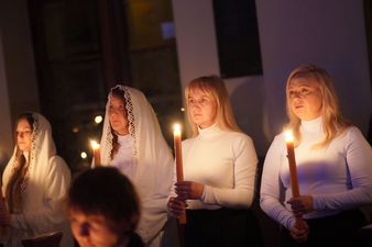 trzy postacie w białych szatach trzymaja zapalone świece