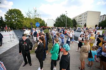 Tłum ludzi zgromadzony na plenerowej uroczystości, z wyróżniającym się na pierwszym planie mężczyzną w czarnym, galowym mundurze górniczym