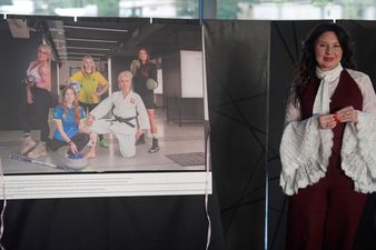 Kobieta w bordowym komplecie z biała koszula stoi przy zdjęciu sportsmenek