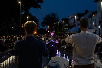 Mężczyźni pozujący na tle fontann perspektywa z tyłu. Z przodu widać tłum widzów