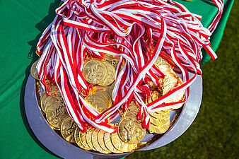 Taca wypełniona złotymi medalami z biało-czerwonymi wstążkami przygotowanymi dla uczestników