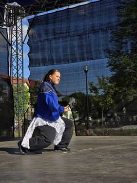 Tancerka w sportowym ubraniu wykonuje dynamiczną pozę podczas występu na zadaszonej scenie