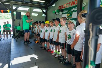Trener wręczający pamiątkowe medale grupie młodych zawodników w białych koszulkach podczas uroczystej dekoracji