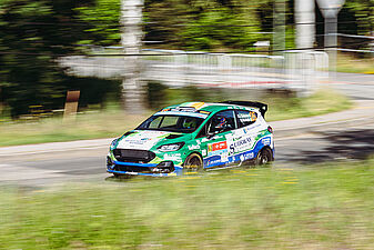 Zielono-biało-niebieski Ford z numerem 26 wchodzi w zakręt na trasie odcinka specjalnego