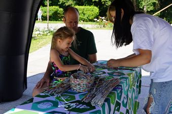 Dziewczynka uczy się robić plecionkę, obok kobieta i mężczyzna