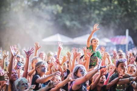 Tłum dzieci z uniesionymi, brudnymi od proszku rękami bawi się na koncercie plenerowym podczas festiwalu kolorów