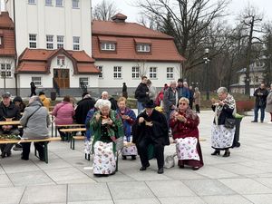 Uczestnicy śniadania wielkanocnego siedzą przy stolikach i jedzą na pierwszym planie kobiety w kolorowych strojach