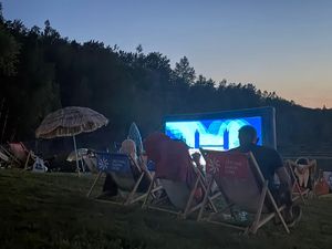 Grupa osób na leżakach i ręcznikach oglądająca film wyświetlany na ekranie 