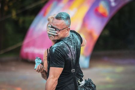 Mężczyzna w czarnej koszulce śmieje się, tuląc kobietę, podczas gdy ich twarze i ubrania pokrywa niebieski pył