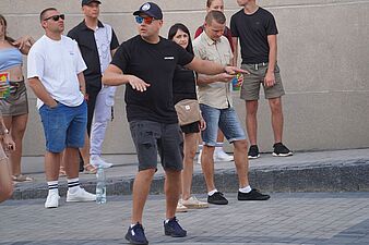 Mężczyzna w kolorowych okularach i czapce tańczący przed tłumem na świeżym powietrzu