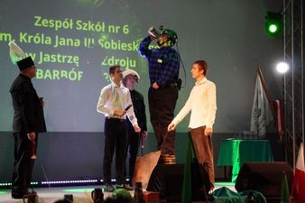 Młody górnik podczas ceremoni pasowania pije napój stojąc na podwyższeniu
