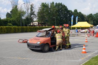 Strażacy w pełnym umundurowaniu ćwiczą rozcinanie i demontaż dachu w pomarańczowym samochodzie osobowym podczas pokazu ratownictwa technicznego