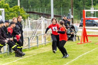 dwie zawodniczki w czarnych spodniach i czerwonych bkuzach przekazują sobie pałeczkę w trakcie sztafety
