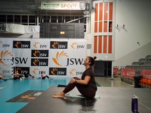 Prowadzaca zajęcia z przypietym mikrofonem w siadzie na podwyższeniu