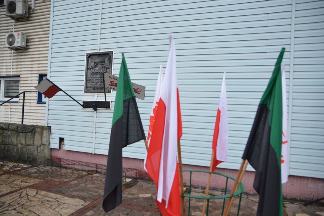 Kopalnia Zofiówka Tablica upamiętniająca wydarzenia 1981 roku, przed nią flagi Polski i górnicze