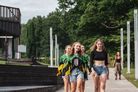 Grupa dziewcząt w sportowych strojach i zielono-żółtych bluzach idąca parkową alejką w stronę kadru