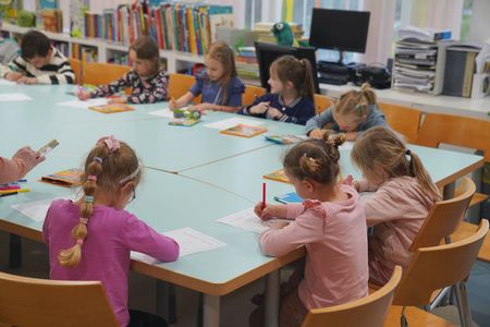 Dzieci siedzą przy stole i malują na kartkach