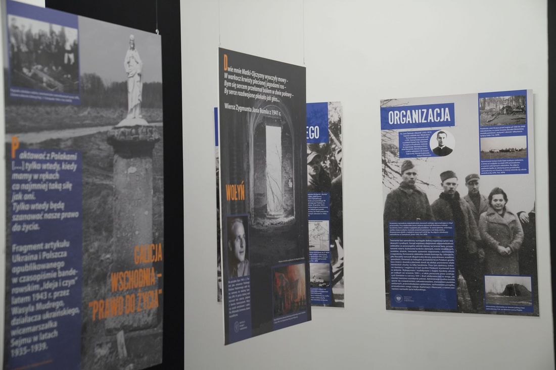 Fragment wystawy historycznej z wiszącymi pionowymi planszami edukacyjnymi, na których znajdują się archiwalne zdjęcia i opisy w języku polskim