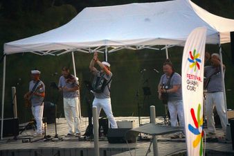 Flaga Festiwalu Górnej Odry po prawej stronie. Na scenie pod namiotem występuje zespół szantowy; akordeonista w marynarskiej czapce unosi ręce w geście klaskania