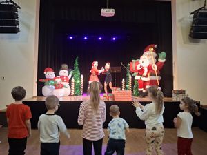 Dzieci bawiące się pod sceną, na które tańczy mikołajowa i elfica,a mikołaj zachęca do zabawy