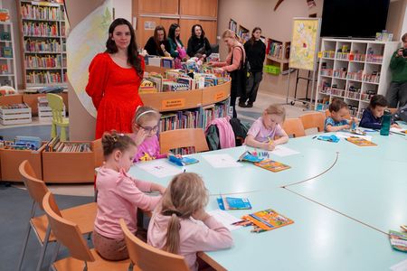 Dzieci siedzą przy stole i malują na kartkach za nimi stoi sonia białek w tle ludzie wybierają książki