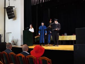 Absolwent w todze i birecie odbiera na scenie dyplom uznania oraz różę z rąk rektora dr. Andrzeja Zduniaka