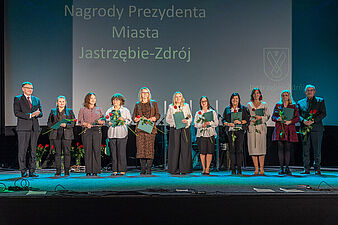 Prezydent Michał Urgoł i drug zastęca prezydenta miasta Andrzej Matusiak wraz z nagrodzonymi nauczycielami stoją na scenie w kinie Centrum podczas uroczystości Dnia Edukacji Narodowej 