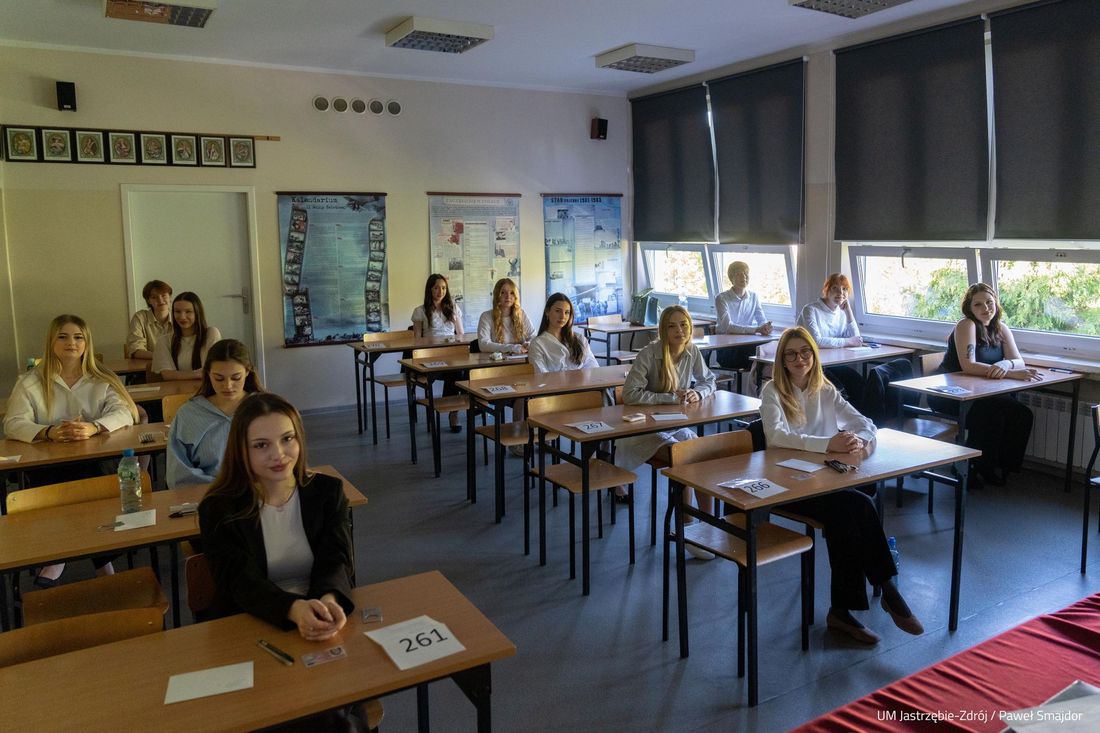 trzy rzędy ławek w nich odświętnie ubrani uczniowie 