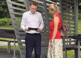 Prezydent czyta dokument w folderze. Obok niego stoi przedstawicielka wyróżnionej placówki, uśmiechając się