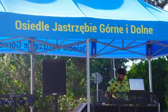 Dj pod niebieskim namiotem z żółtym napisem Osiedle Jastrzebie Górne i Dolne.
