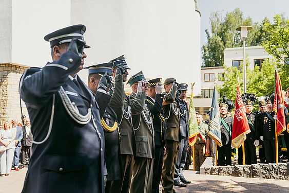 Wojskowi w galowych mundurach stoją na baczność i salutują