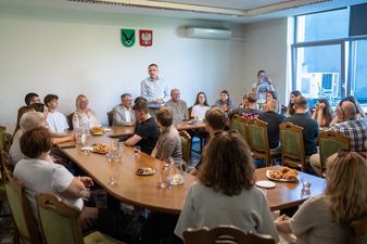 Spotkanie młodzieży i dorosłych przy dużym stole w sali konferencyjnej. Michał Urgoł Prezydent Miasta przemawia do zebranych