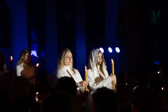 kobiety w bieli kroczą nawą trzymając zapalone świece