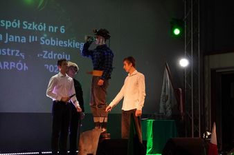 Młody górnik podczas ceremoni pasowania pije napój stojąc na podwyższeniu