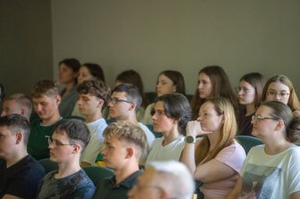 Profil skupionych młodych osób siedzących obok siebie w ławkach sali wykładowej