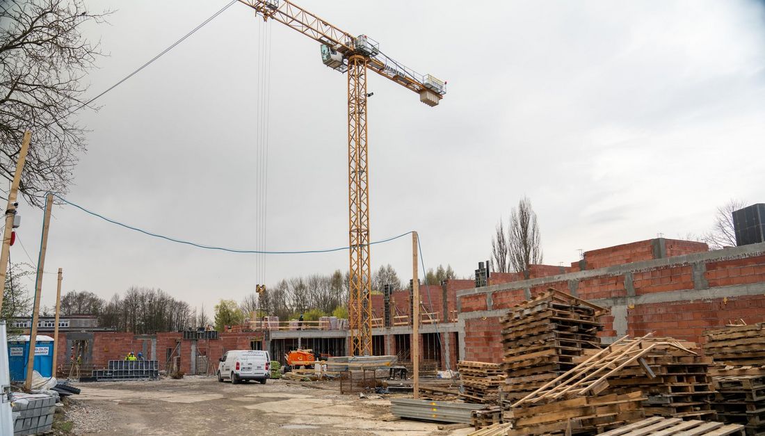 Plac budowy przedszkola na ulicy kaszubskiej widać mury budynku żuraw stertę drewnianych palet i samochód