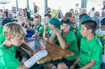 Młodzi zawodnicy UKS Orzeł Moszczenica siedzący przy ławach podczas wspólnego posiłku w trakcie festynu klubowego