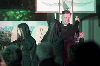 Kobieta ubrana na czarno wręcza aktorowi grającemu rolę księdza Machy kadzidło, scena podświetlona na zielono