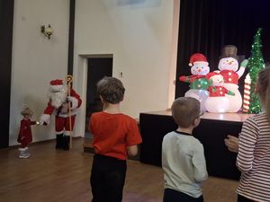 Dzieci przy scenie, w rogu mała dziewczynka wita się z mikołajek