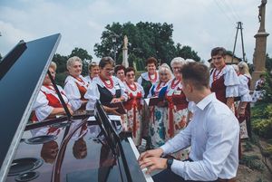 Mężyczyna gra na fortepianie. w tle śpiewają kobiety w strojach ludowych
